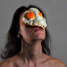 顔の上に生肉、みかん、生クリーム、目玉焼きなどを載せて撮影したアート作品「On Your Face」
