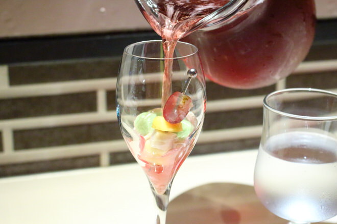 食前酒。お重の花とフルーツに、ぶどうジュースをスパークリングワインで割ったものを注ぐ